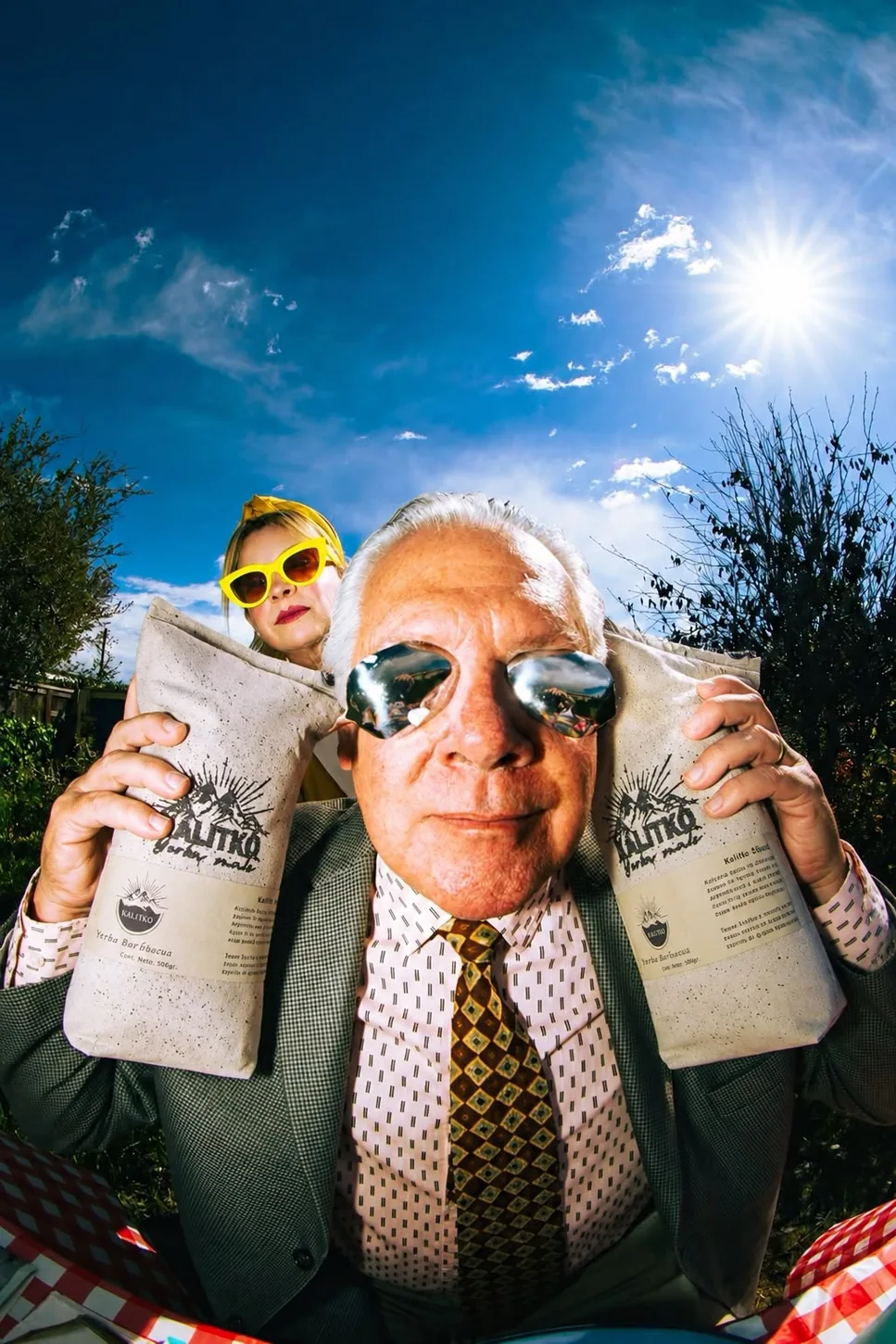 Imagen de campaña Kalitko: un personaje mayor con anteojos de sol sostiene dos paquetes de yerba mate